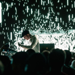 Man in baeball cap playing guitar during a concert with light show behind him