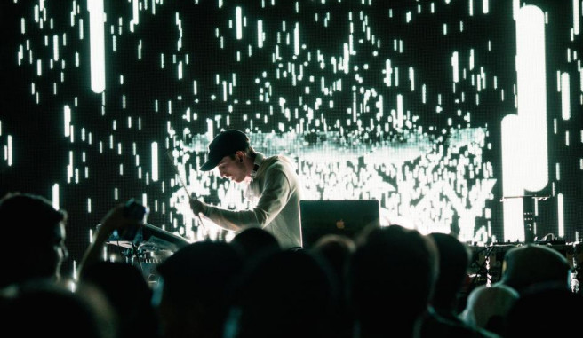 Man in baeball cap playing guitar during a concert with light show behind him