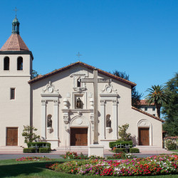 Mission Santa Clara de Asis with blue sky vibrant colorful flowers and palm trees