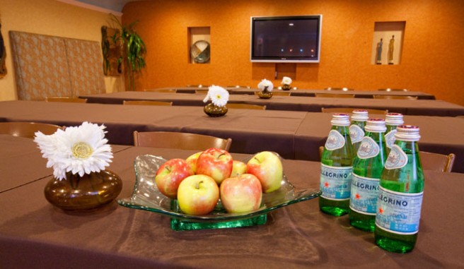 meeting space, containing rows of brown table clothed tables and chairs with flowers and snacks Header
