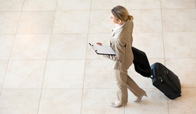 business women, in tan pant suit, walking with suitcase Header