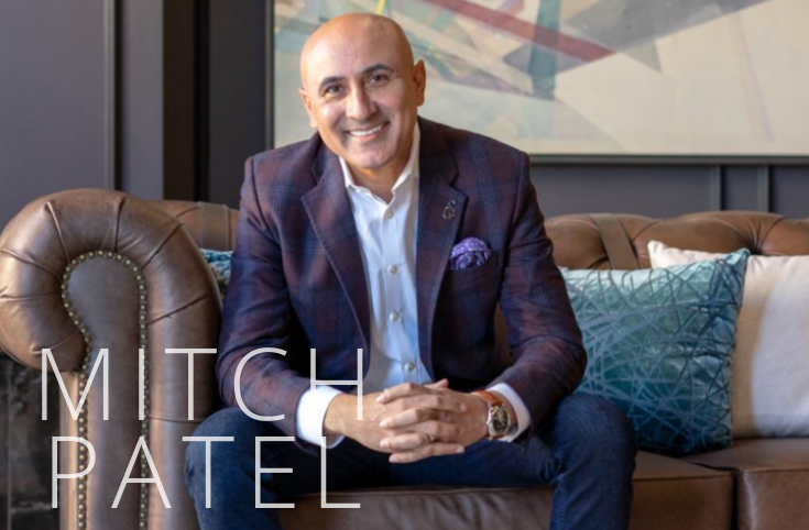 an image of a man in a suit sitting on a sofa smiling with the words mitch patel