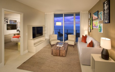 1 bedroom ocean view living room. Couch and 2 chairs, television mounted on the wall, adjacent room