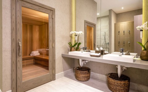Emena Spa Sauna with adjacent sinks. Room has earth tone tiles and counter tops