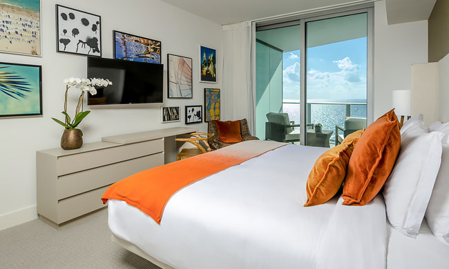 One Bedroom Suite, with dresser, desk, mounted tv, queen size bed, balcony with ocean view