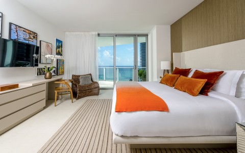 one bedroom suite, with dresser and desk. Mounted TV and queen sized bed, balcony with ocean view