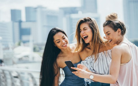 Three women laughing over something on a phone 