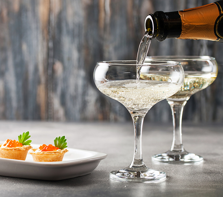two coup glasses of champagne being served with a plate of two amuse bouche