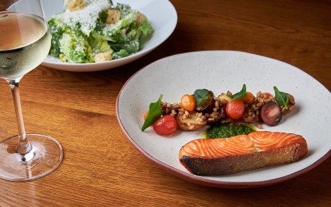 a dish of salmon and vegetables with a side salad and a glass of white wine