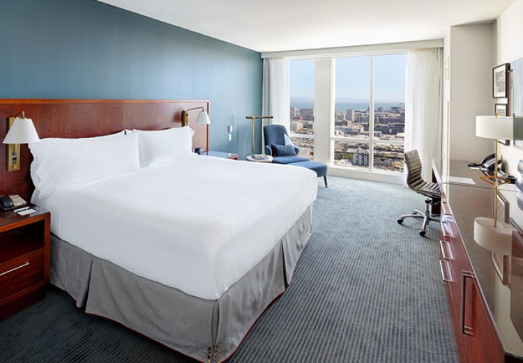 guest room with white linens and floor to ceiling windows with a view of the city