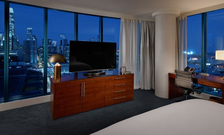 large room with a bed, tv, and view of the city lights at night
