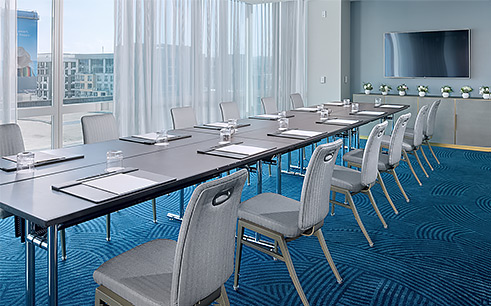 conference room at a hotel with blue carpet, long conference table with chairs, and a tv on the wall