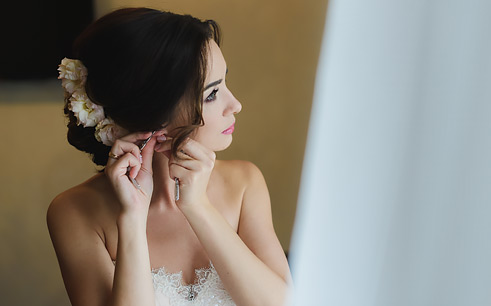 bride standing by a window putting on her earrings