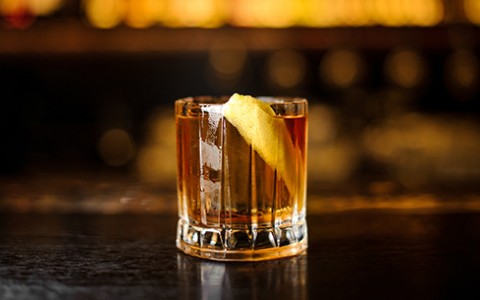 Clear brown cocktail in a rocks glass garnished with a lemon peel.