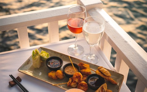 Appetizers and glass of wine on a linen table overlooking the ocean.