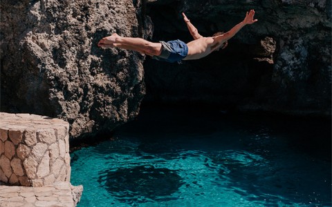 A man in the air jumping into a pool below and a woman floating.