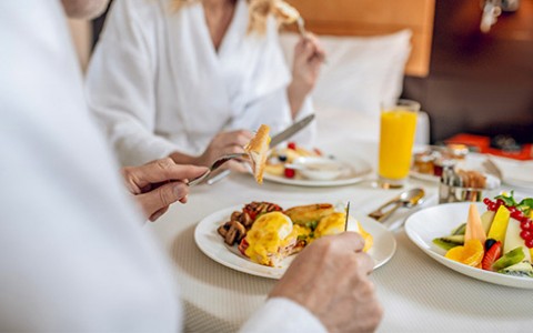 Male and female enjoying eggs benedict and fresh fruit with a glass of fresh squeezed orange juice.
