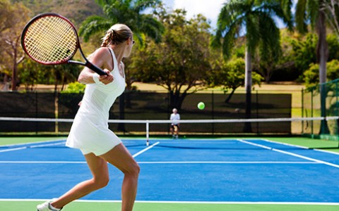 Woman wearing a white tennis tank and skirt getting ready to hit tennis ball to the other side of the court.