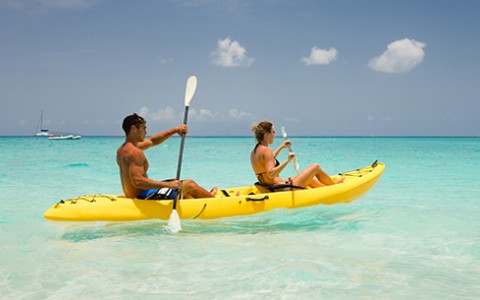 Male and female in a yellow kayak in the clear blue water with the sun shining.