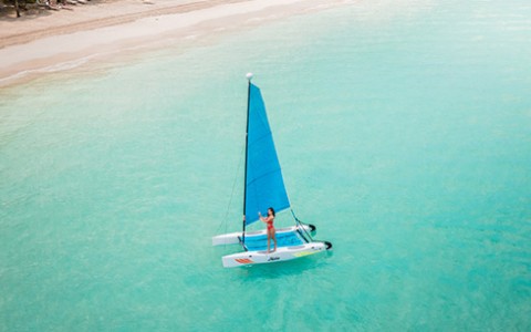 Woman guiding a blue and white sailboat to the shore during the day.