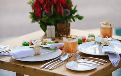 Light oak colored table setup for dinner with two cocktails served in a rocks glass at dusk.