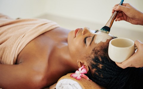 Female laying down with her head propped on rolled towels getting a mask painted on her face during a spa service.
