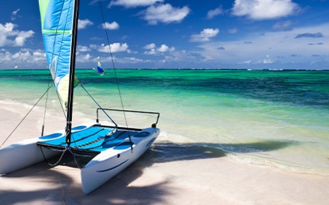 A white and blue sailboat beached on the sand during the day with the sun shining brightly.