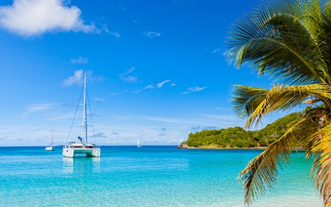 Three sailboats anchored in the crystal clear blue water during the day with the sun shining above.