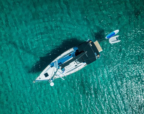 Drone shot of an anchored white sailboat with two smaller boats tied to the back.