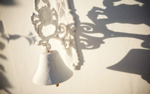A white bell with a crab decoration and its shadow cast on the wall behind it.