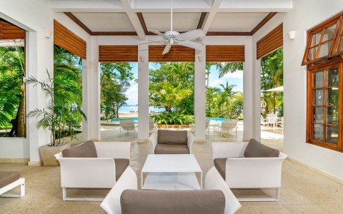 Outdoor seating with light brown cushions and a white coffee table with a view of the pool and beach in the background.
