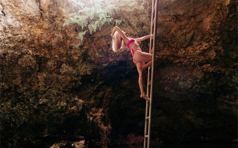 Woman wearing pink bikini climbing up a wooden ladder from the water to the land above.