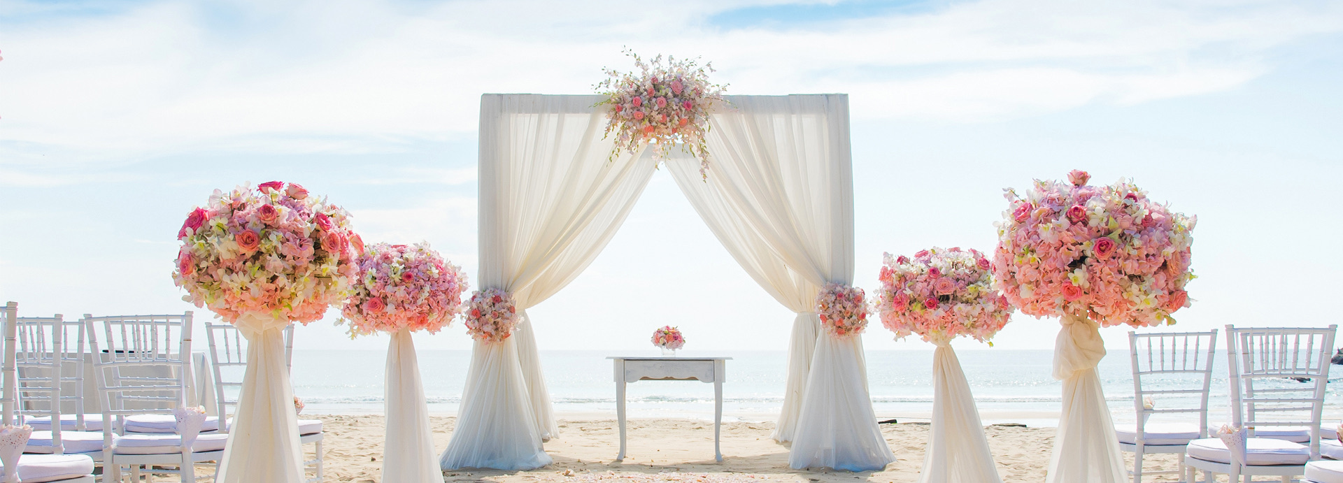 Wedding setup on the beach with white canopy over the alter and the ocean in the distance during the day.