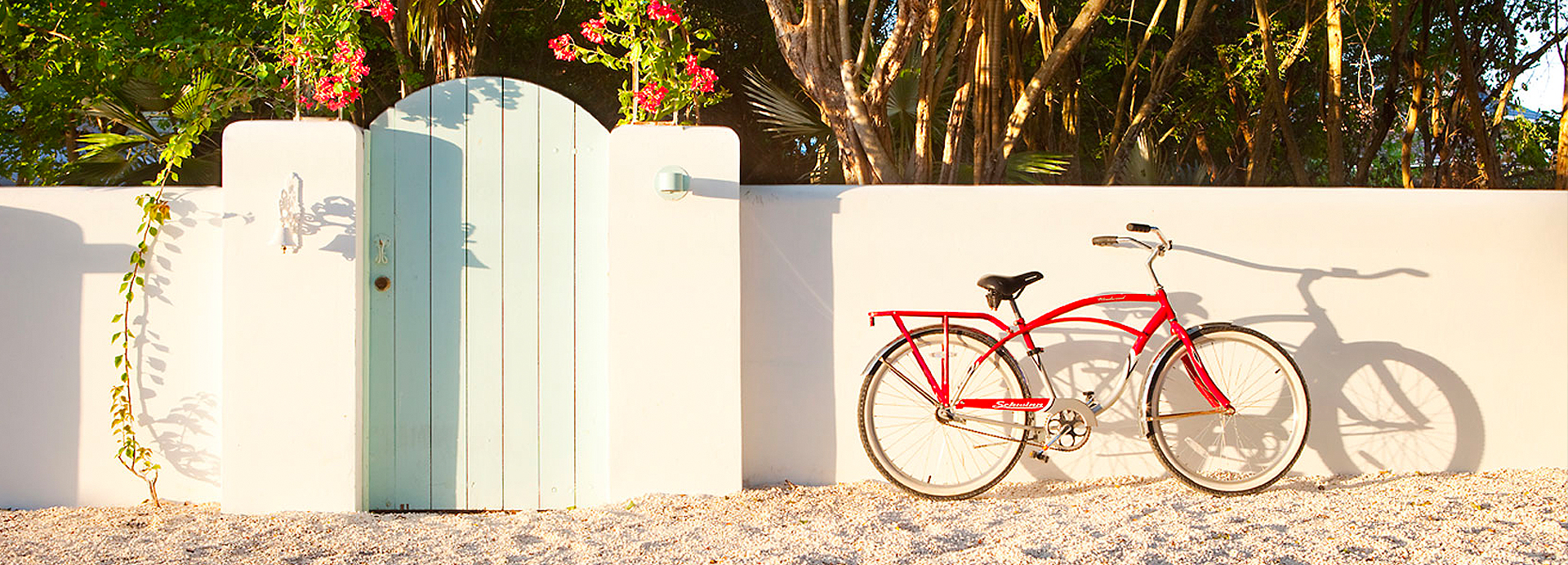 Red bicycle propped against beige colored concrete wall with beige gravel underneath.