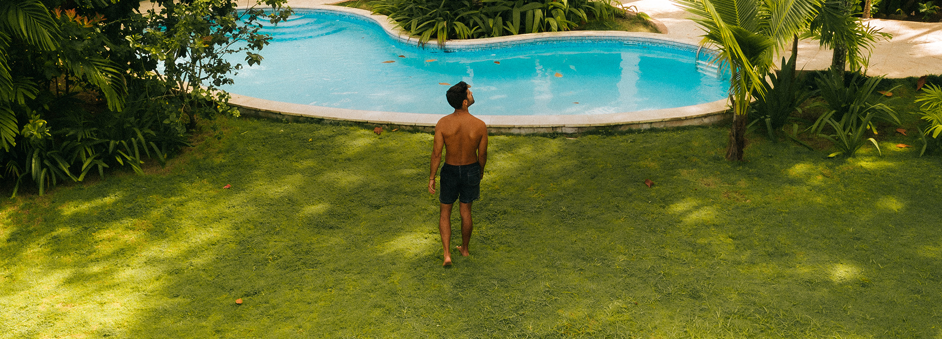 man walking in the grass by a pool