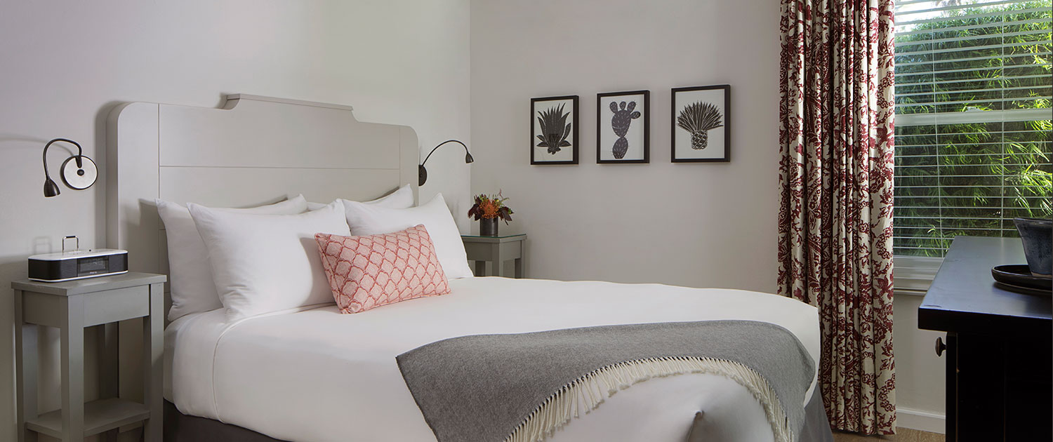 guest bedroom with white sheets, gray throw blanket, coral decorative pillow, ceiling fan, and two small side tables