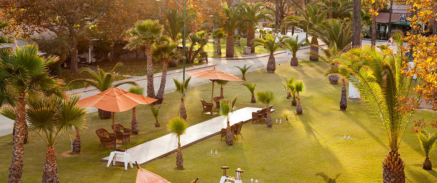 a shuffleboard area in the middle of a grass terrace with orange umbrellas and brown lawn chairs