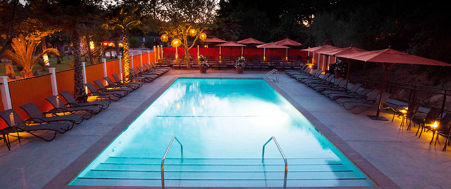 rectangular pool area secluded by trees with lounge chairs and orange umbrellas
