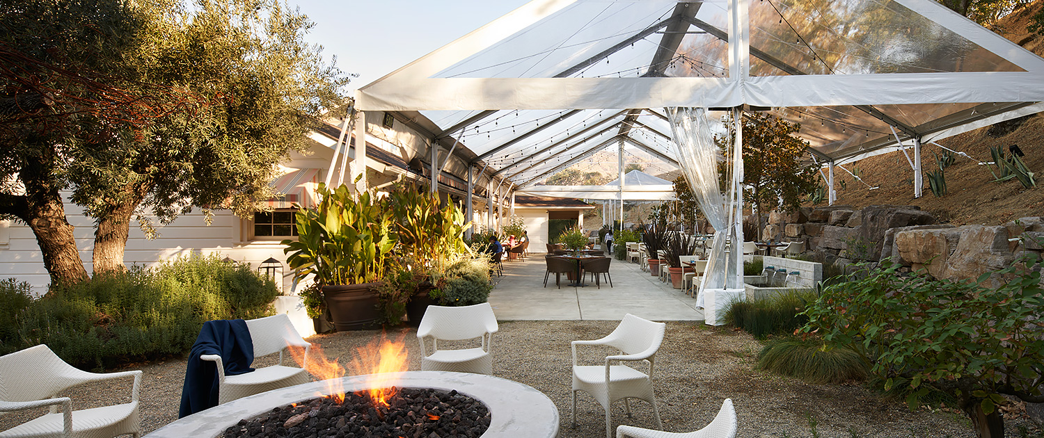 outdoor dining area with large circular fire pit and tent