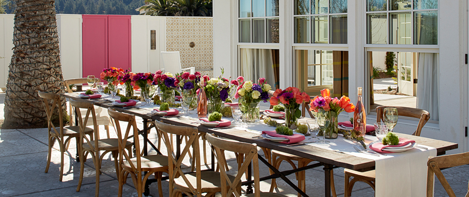 long dining table on an outdoor patio decorated with bright colored flower centerpieces