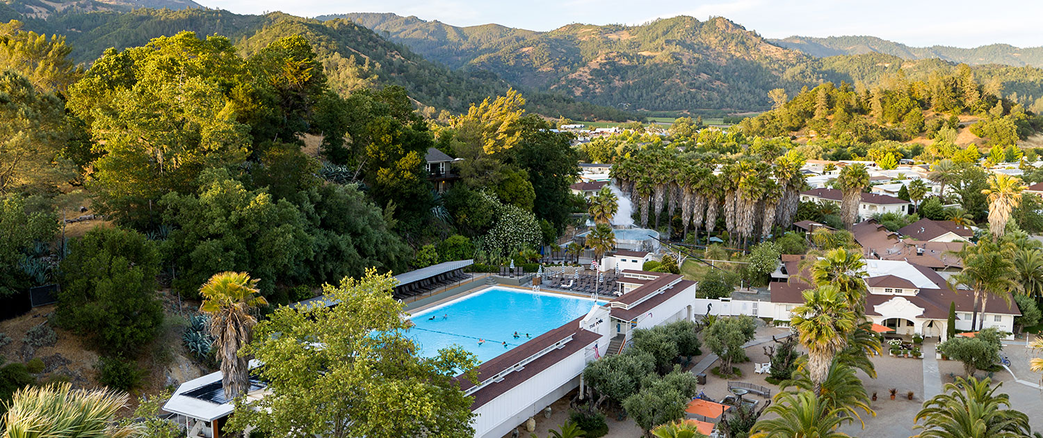 overhead view of the pool area, surrounding resort buildings, and a view of the mountains in the distance