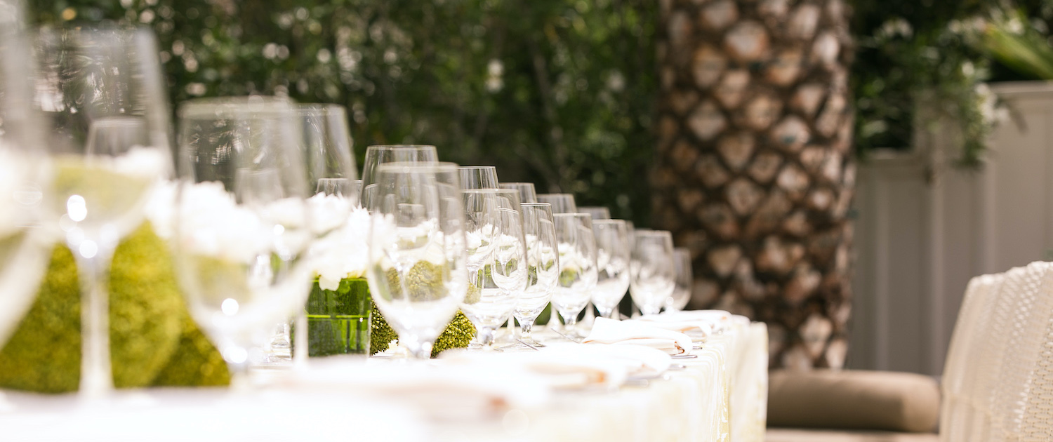long dining table set for wedding event with empty wine glasses and white chairs