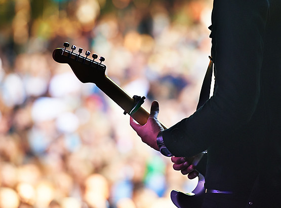Silhouette of man playing guitar on stage with crowd in the background