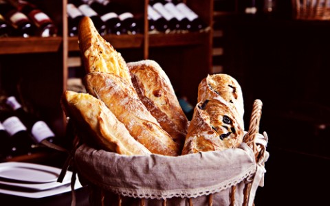 fresh bread in basket with bottles of wine on background