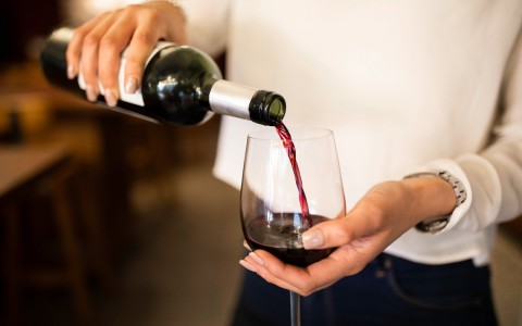 person pouring red wine into glass