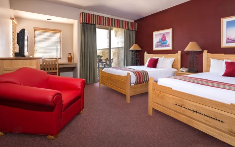 hotel room with 2 beds and a bright red sofa chair