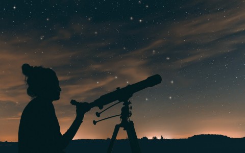 woman looking at night sky through a telescope
