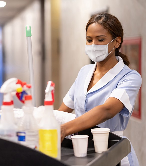masked woman getting grabbing items from cleaning cart