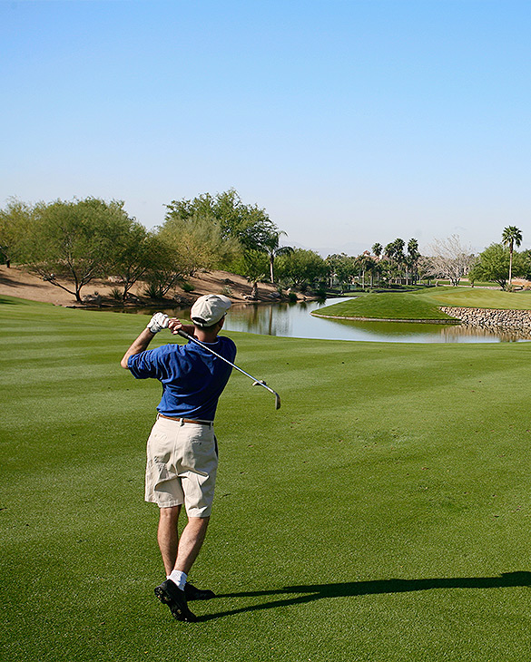 person swinging back golf club with a view of water feature