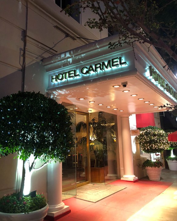 exterior of Hotel Carmel with trees on either side of glass door entrance